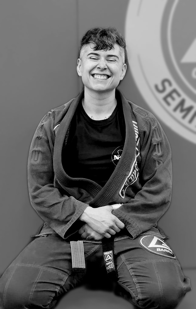 Professor Sammy Rider, black belt instructor at Gracie Barra Seminole, kneeling in their gi in front of the Gracie Barra Seminole gym wall